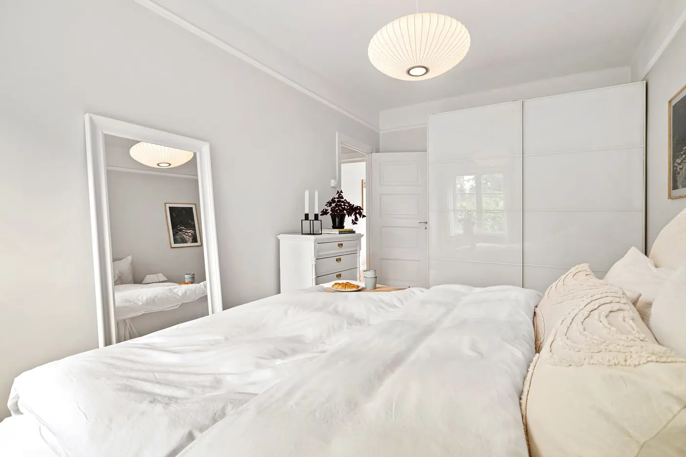 Une chambre blanche avec un grand lit, un miroir et une commode
