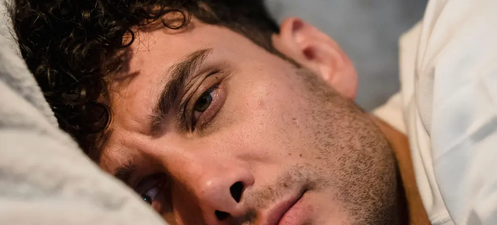 Un homme allongé, le visage tendu, les yeux ouverts, la joue contre l'oreiller