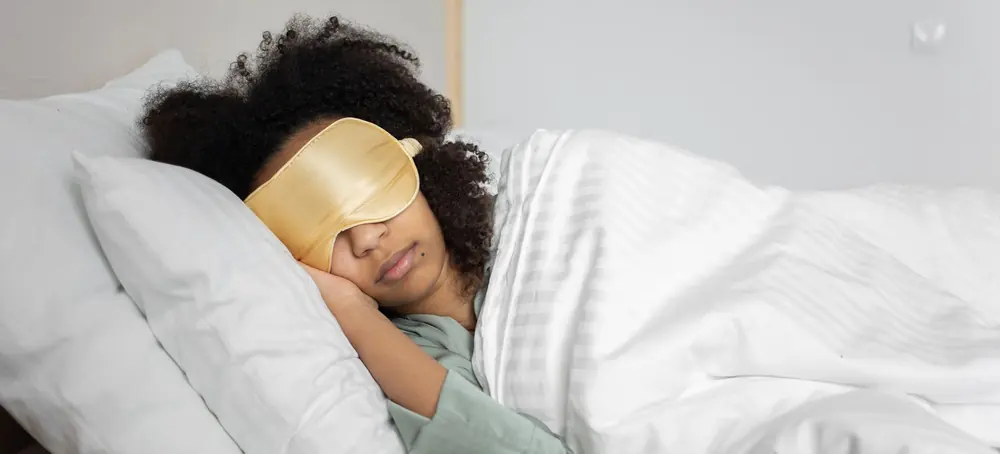 Une femme endormie sous un masque de sommeil doré, dans un lit aux draps blancs