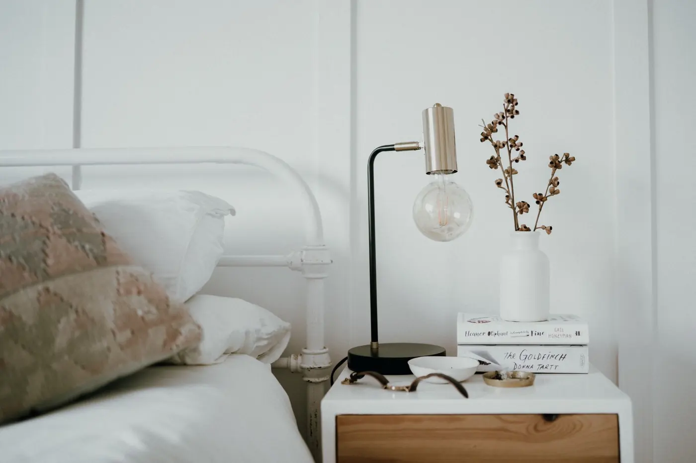 Une table de chevet avec une lampe, à côté d’un lit aux oreillers clairs
